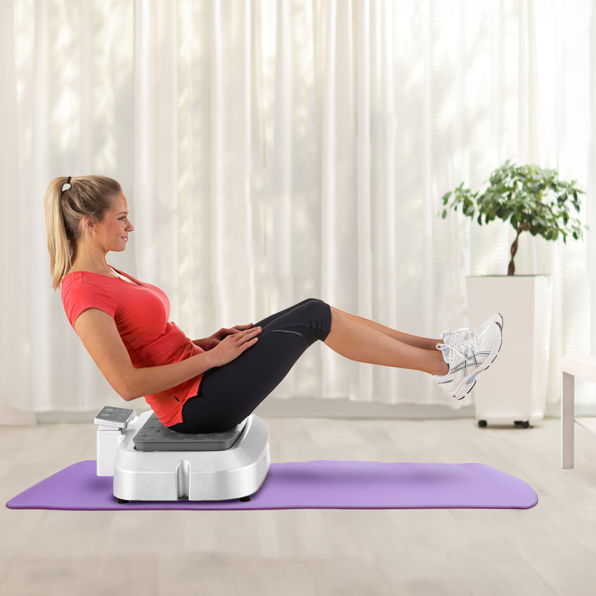 A woman in workout clothes balances with bent knees and feet raised on a Reviber Plus Oscillating Vibration Plate Exerciser by Reviber, set on a purple mat in a bright room with light curtains and a potted plant.