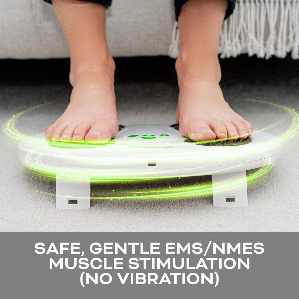 Close-up of bare feet on the Reviber Circulation Stim by Reviber, emitting green light near a gray sofa. Safe, gentle EMS/NMES muscle stimulation (no vibration) for active recovery and improved lower leg strength.