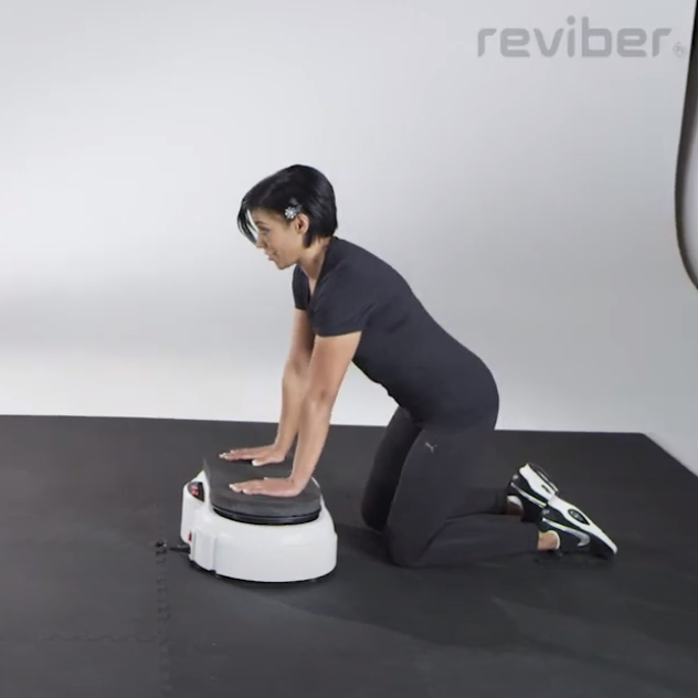 Wearing black athletic wear, a person kneels on a mat and presses their hands onto a white Reviber Fusion Workout Cushioning Block by Reviber, making it ideal for seated exercises in a studio setting.
